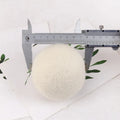 Assorted sized wool drying balls next to a beige cotton drawstring storage bag on a wooden surface.