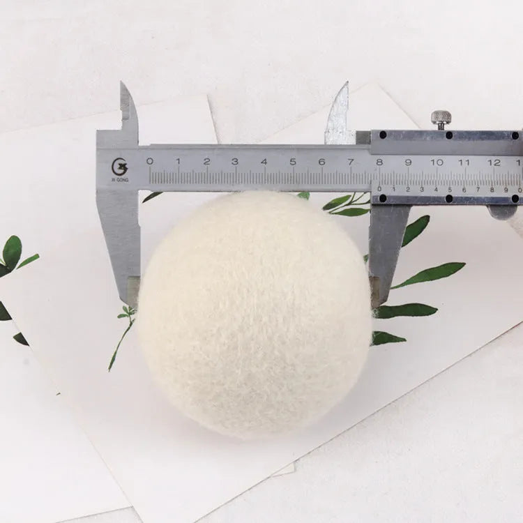 Assorted sized wool drying balls next to a beige cotton drawstring storage bag on a wooden surface.