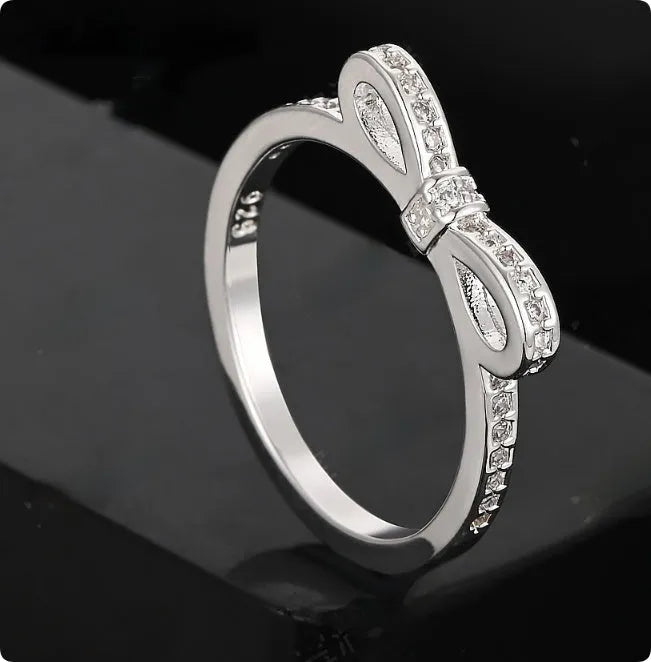 Silver coloured bow-shaped ring with rhinestone and zircon crystal details on a model finger.