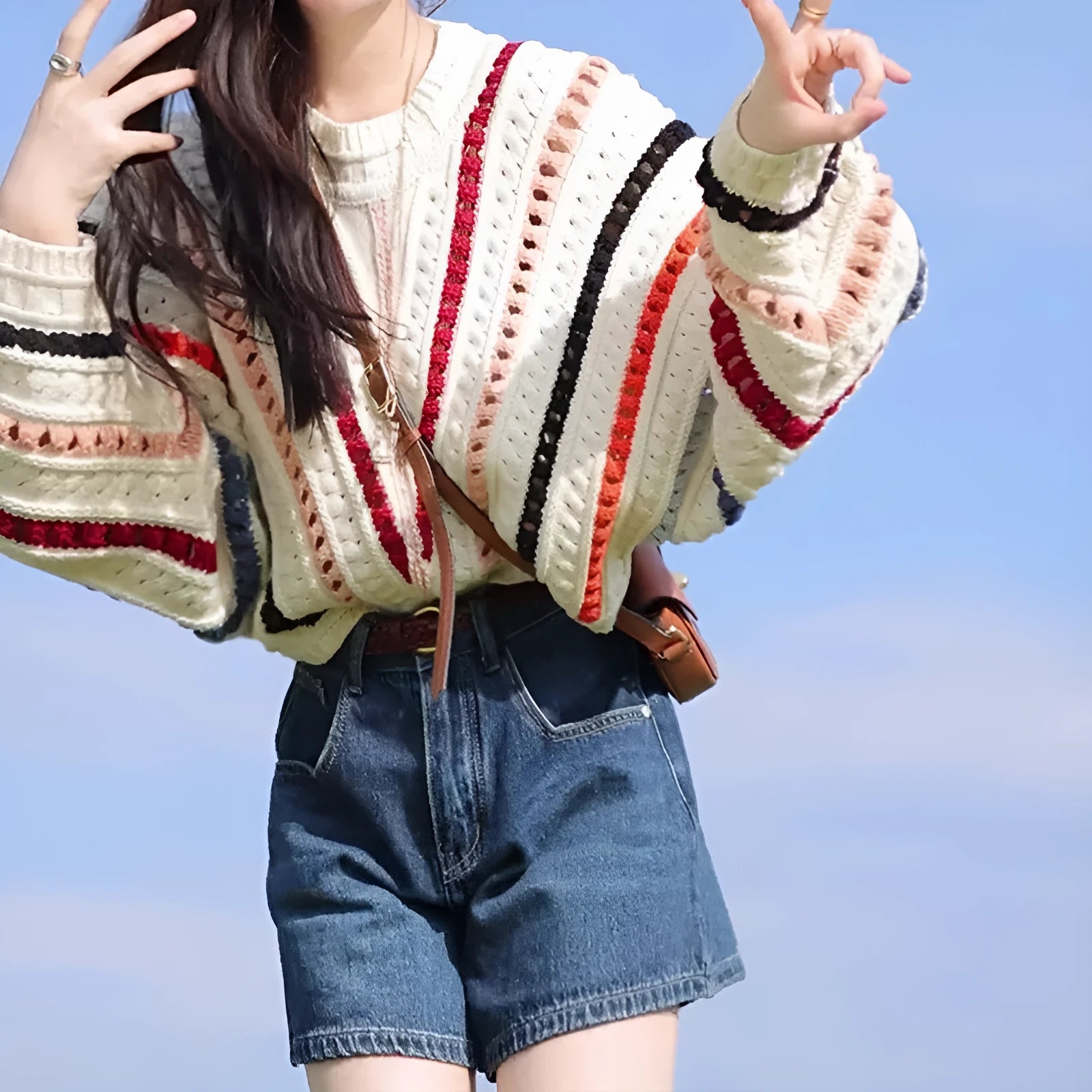 A woman's rainbow striped loose knit sweater with batwing sleeves on a hanger.