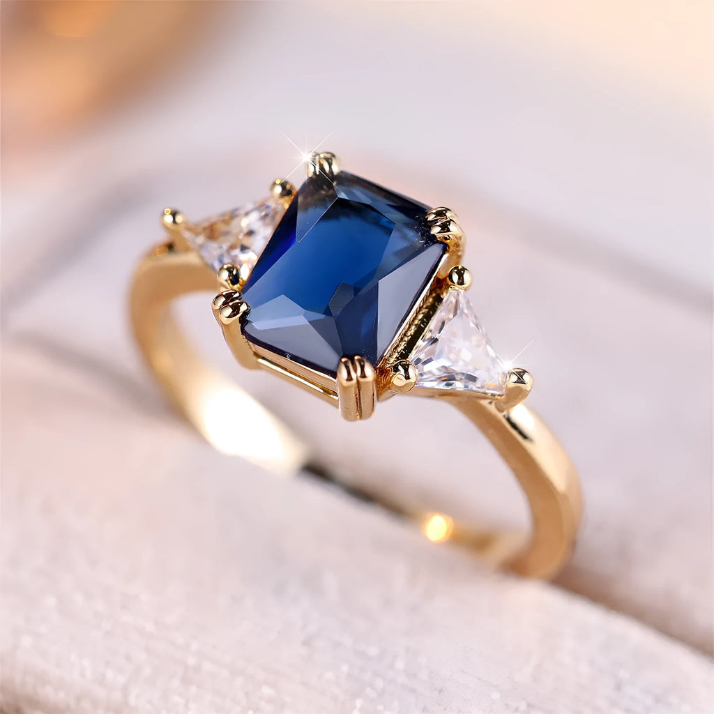 Gold sapphire blue rectangular copper ring for women on a plain background