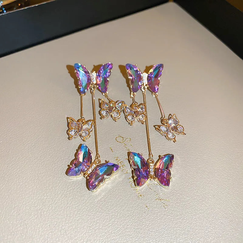 A pair of silver and blue purple butterfly tassel earrings with crystal flowers and droplet pendants.