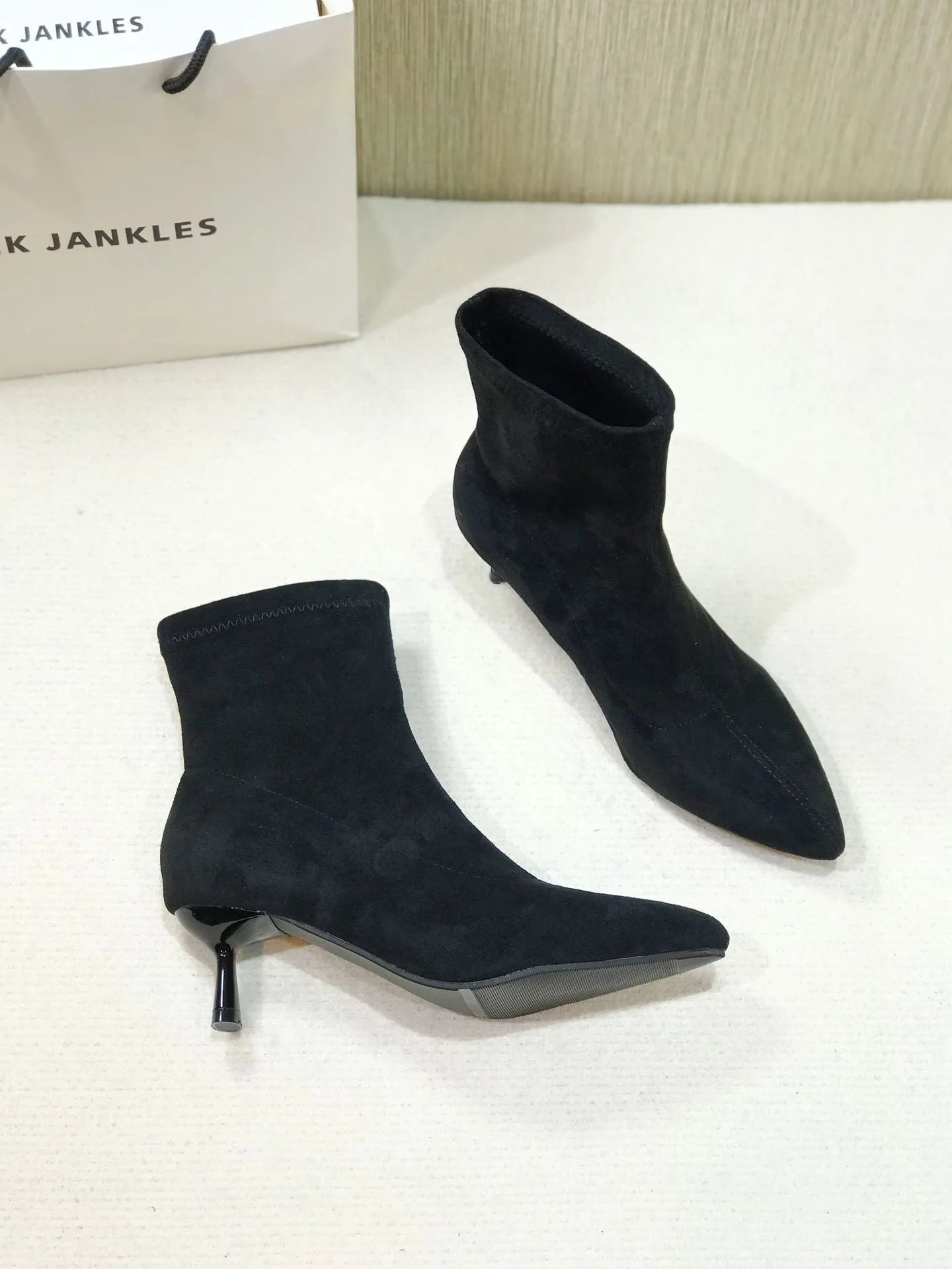 Black microfiber ankle boots with a stiletto heel and pointed toe on a mid-calf sock.