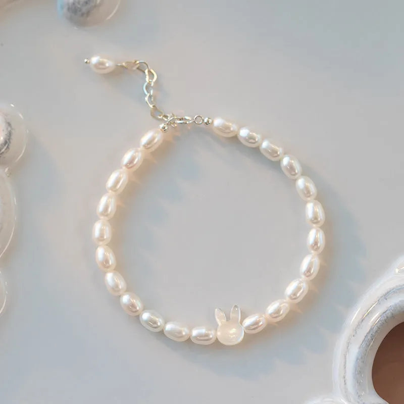 White shell pearl elastic bracelet with 925 silver rabbit charm on wrist showing rice-shaped beads and adjustable closure