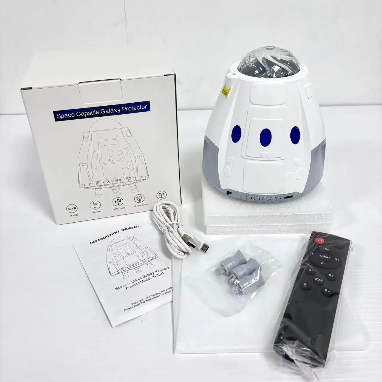 Space capsule shaped USB galaxy projection lamp with remote control on a surface.