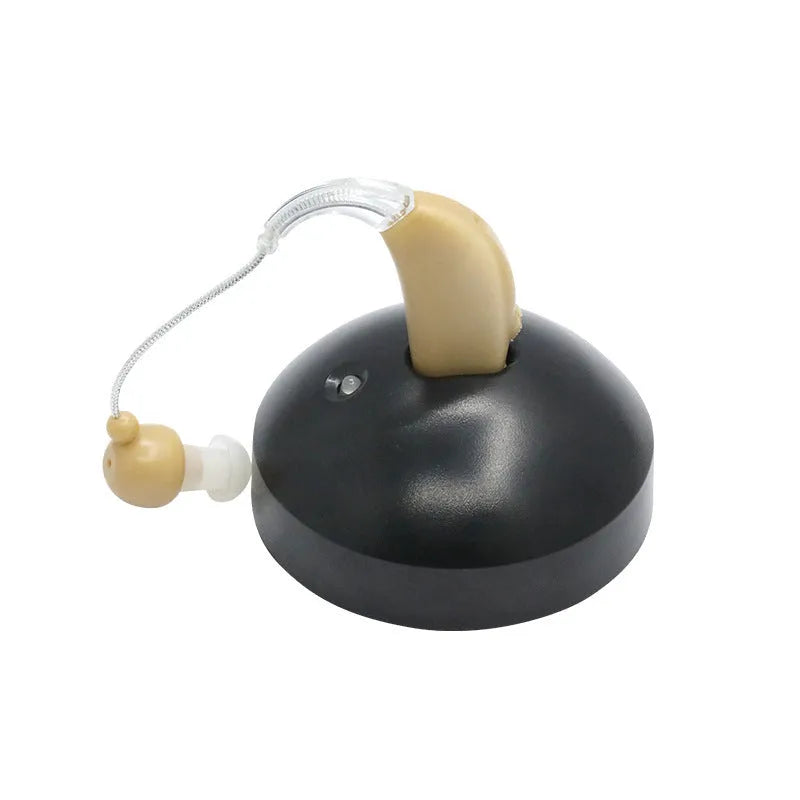 Black silicone rechargeable hearing aid amplifier with charging cable on a table.