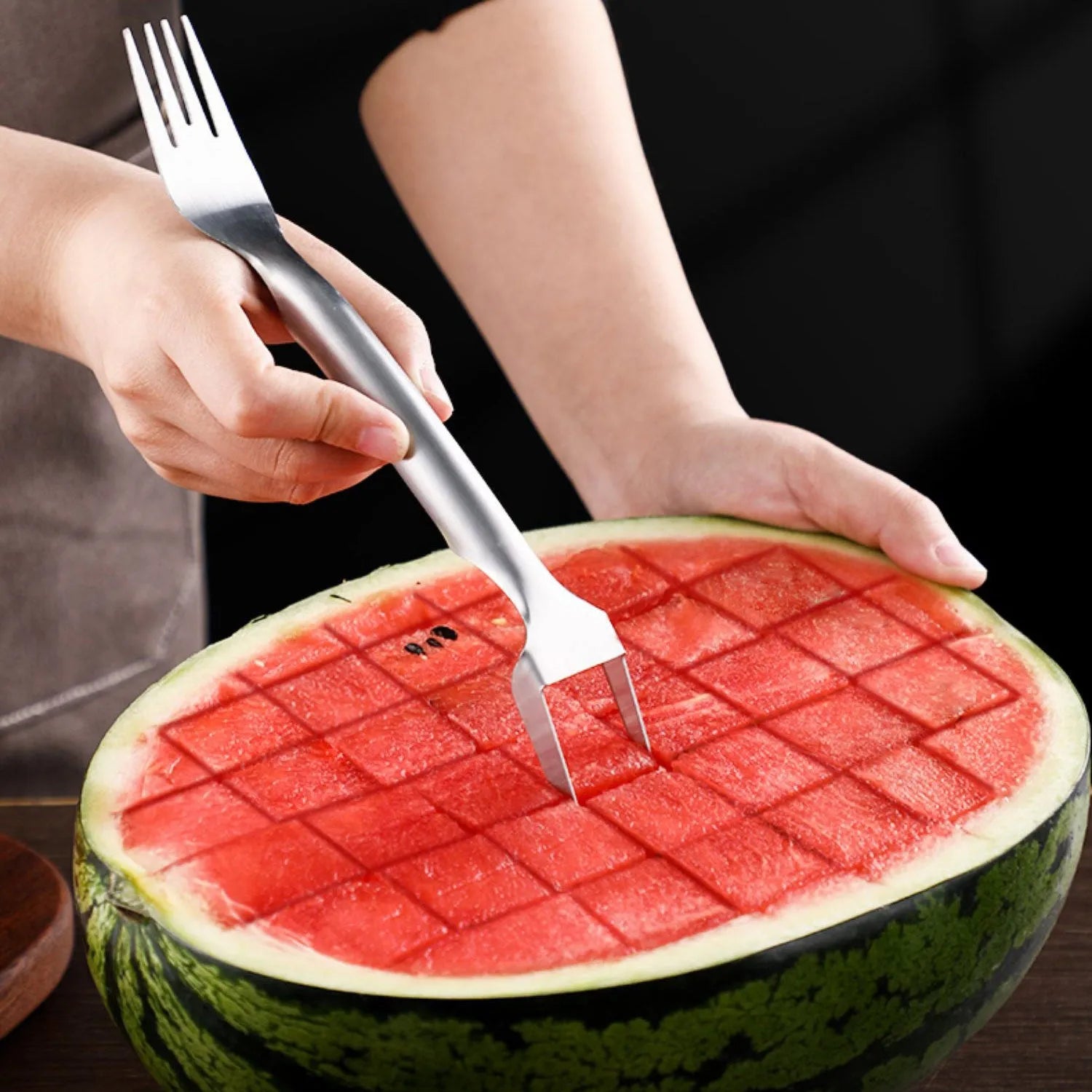 Silver stainless steel watermelon slicer and serving fork with a long handle on a kitchen surface