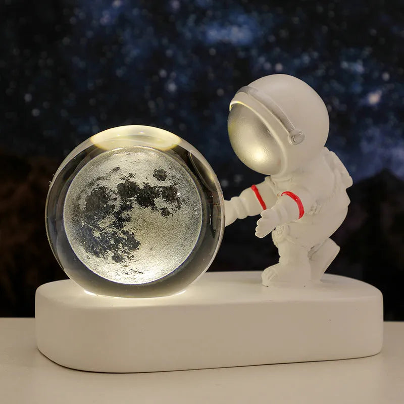 Small clear resin ball night light with glowing astronaut and galaxy scene inside on dark surface