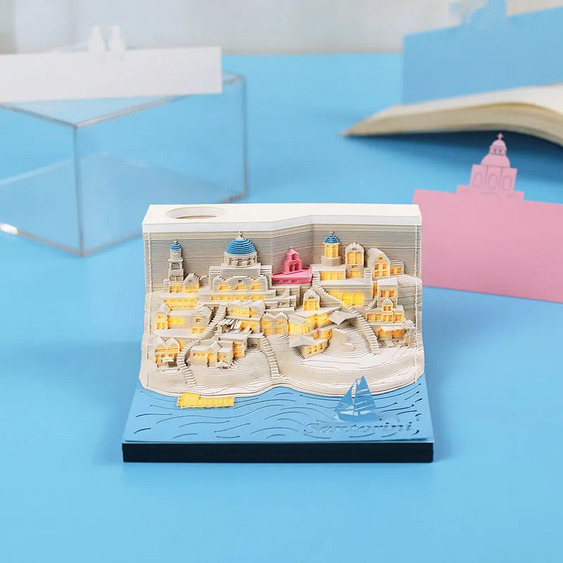 Assembled Santorini beach 3D paper model notepad with decorative lighting on a desk.
