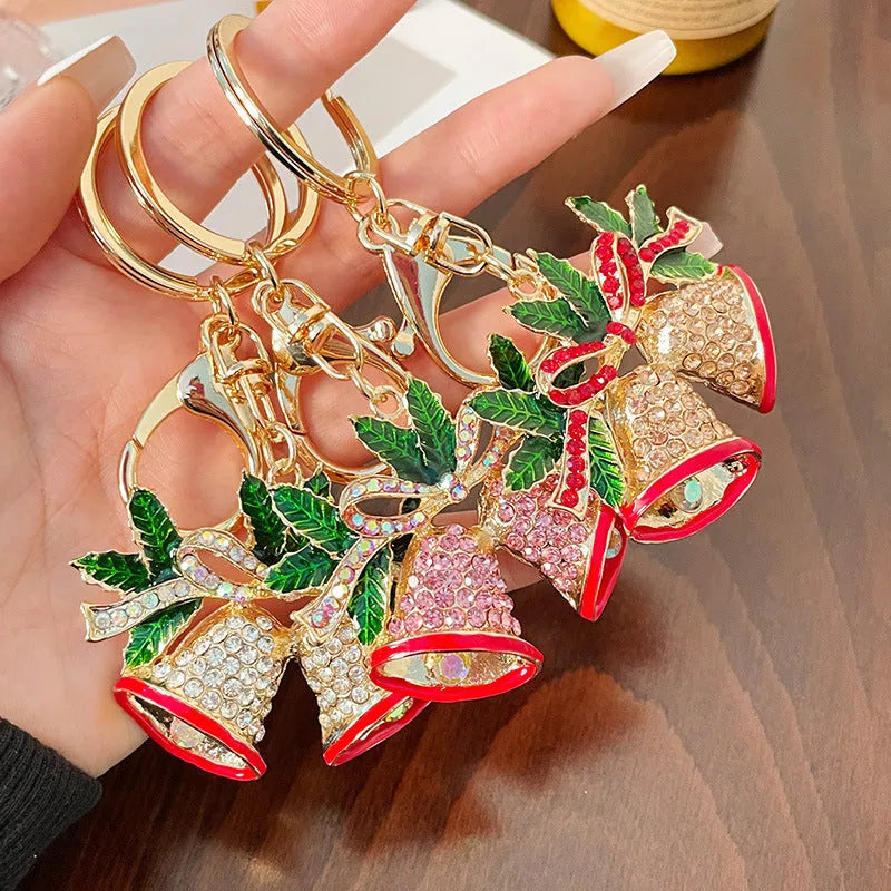 Diamond studded Christmas bell shaped keychain in metal, white diamond colour, on a festive background