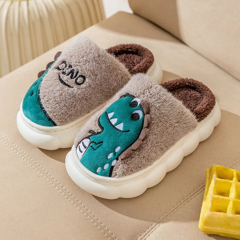 A pair of plush grey dinosaur print slippers with a thickened sole, shown on a wooden floor.