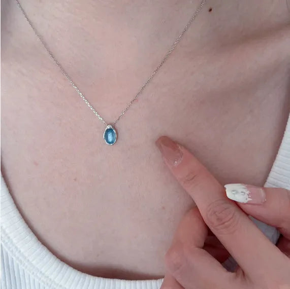 Close-up of a navy blue geometric water drop pendant on a platinum-colour adjustable cross chain necklace.