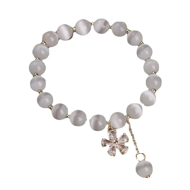 White cat's eye stone women's bracelet with flower and tassel charms on a morganite safety buckle.