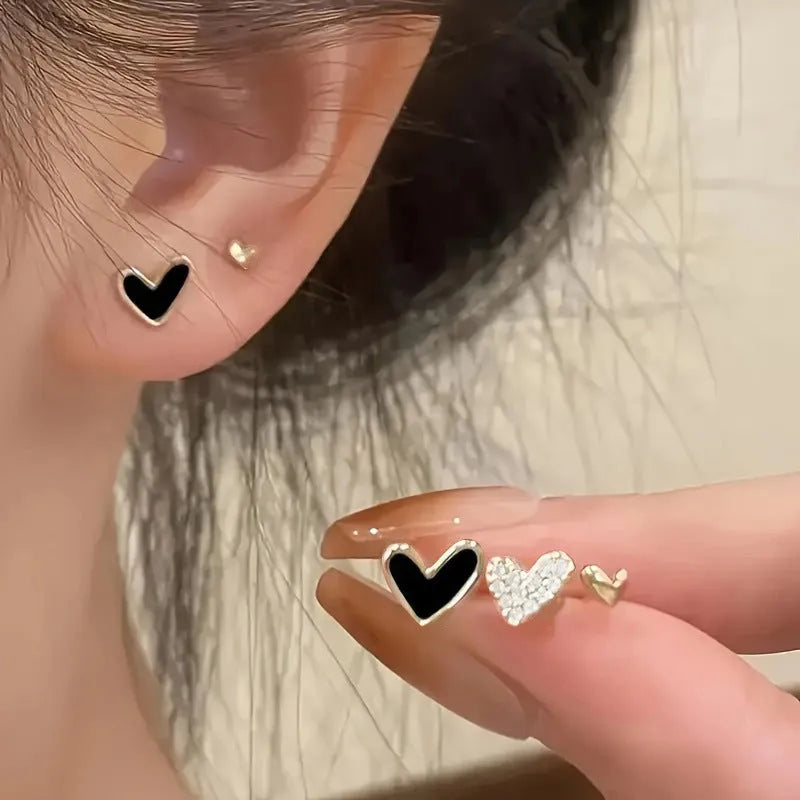 Three pairs of women's heart-shaped earrings in gold, black, black and white, and pink colours