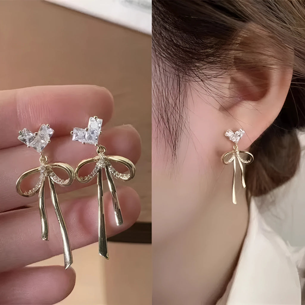 Pair of alloy bow tie ear studs with love heart zircon centre on light background