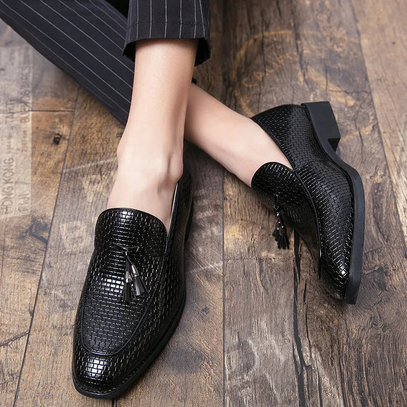 Men's black slip-on leather loafers with a pointed toe and tassel detail on a white background.