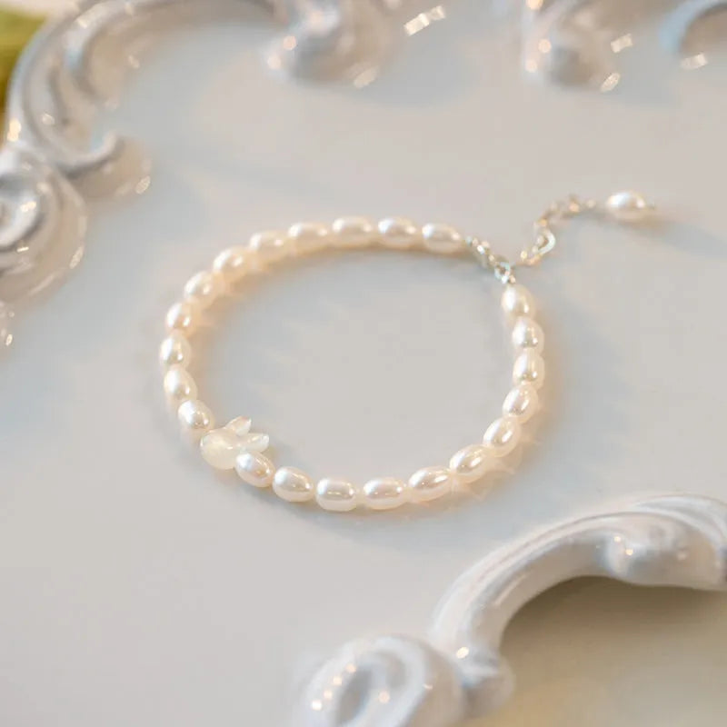 White shell pearl elastic bracelet with 925 silver rabbit charm on wrist showing rice-shaped beads and adjustable closure
