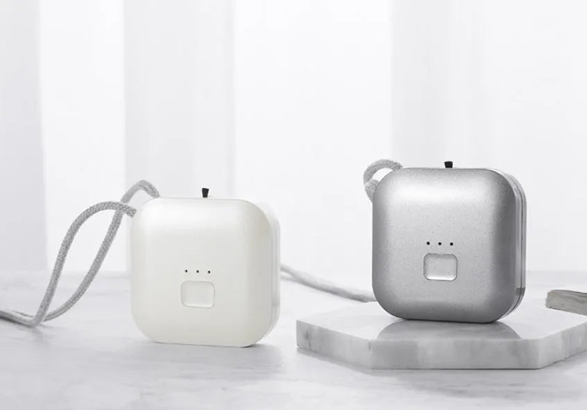 Compact pink USB portable air purifier necklace on a table with charging cable.