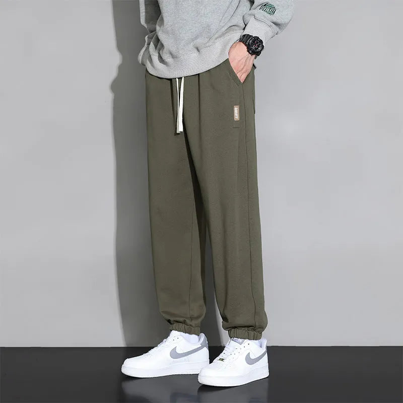Men's grey loose-fit cotton blend sports trousers with a drawstring waistband on a hanger.