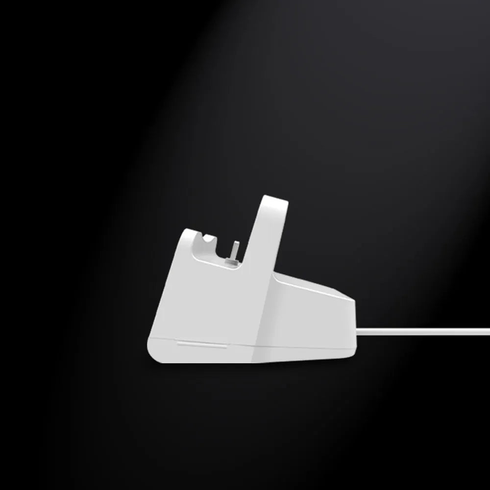 White headphone charging base station on a desk, holding a pair of over-ear headphones.