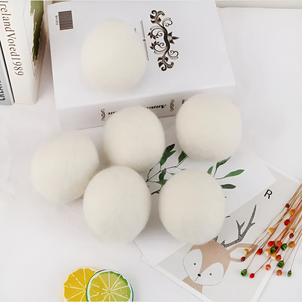 Assorted sized wool drying balls next to a beige cotton drawstring storage bag on a wooden surface.