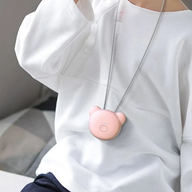 Compact pink USB portable air purifier necklace on a table with charging cable.