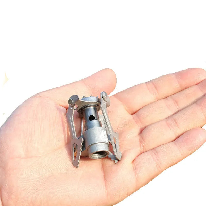 Portable metal propane camping stove with one-piece furnace design on a outdoor surface.