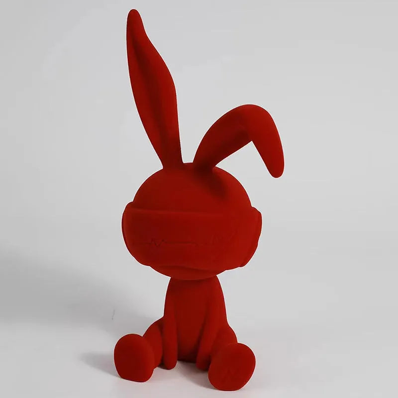 Green resin blindfold rabbit table ornament with suede details on a wooden shelf.