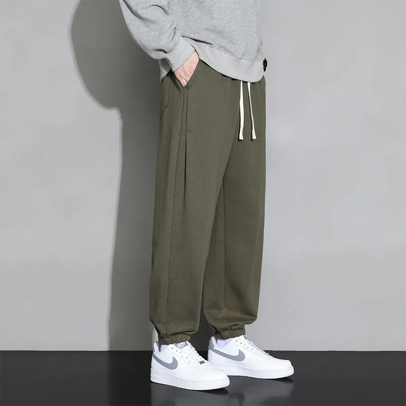 Men's grey loose-fit cotton blend sports trousers with a drawstring waistband on a hanger.
