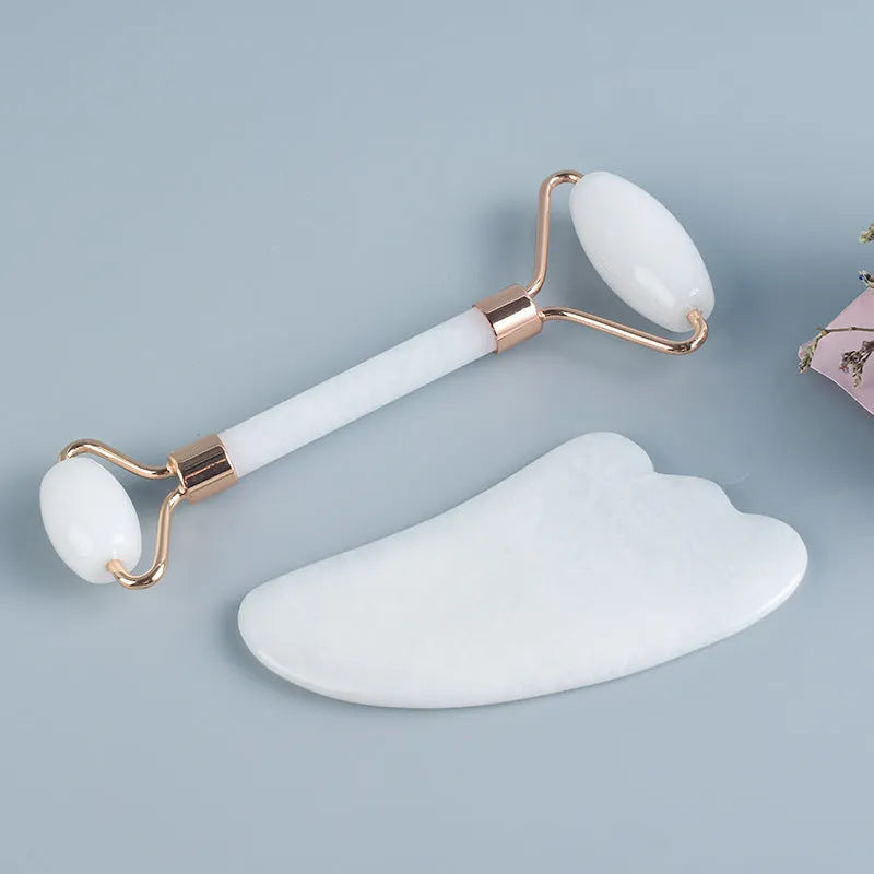 White jade facial roller and gua sha scraping tool set presented on a wooden board.