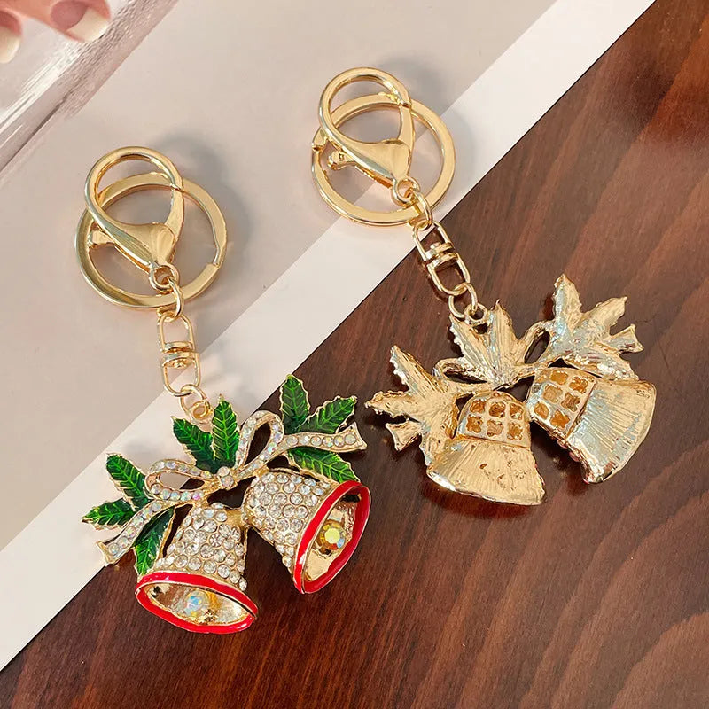 Diamond studded Christmas bell shaped keychain in metal, white diamond colour, on a festive background