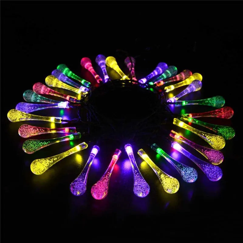 Water drop shaped solar LED fairy lights hanging outdoors with solar panel and ground spike.