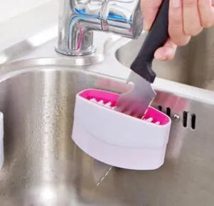 Blue kitchen cleaning brush with slots for utensils and a suction cup on a white wall.