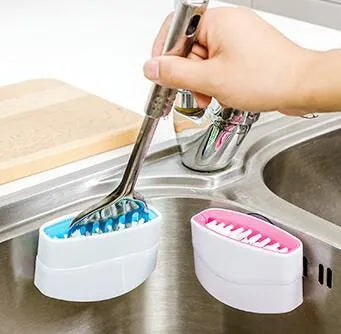 Blue kitchen cleaning brush with slots for utensils and a suction cup on a white wall.