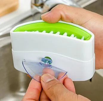 Blue kitchen cleaning brush with slots for utensils and a suction cup on a white wall.