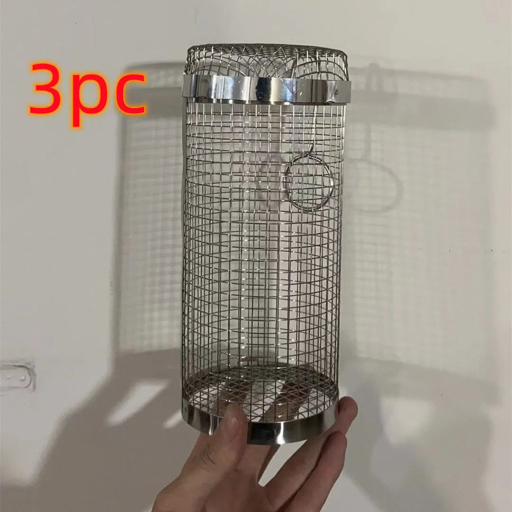 Round silver metal rolling barbecue basket with wire mesh and a hook, shown with vegetables inside on a grill.