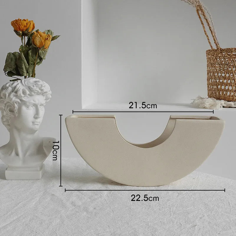 Unglazed matte ceramic vase for dried flowers in a neutral colour on a wooden table.