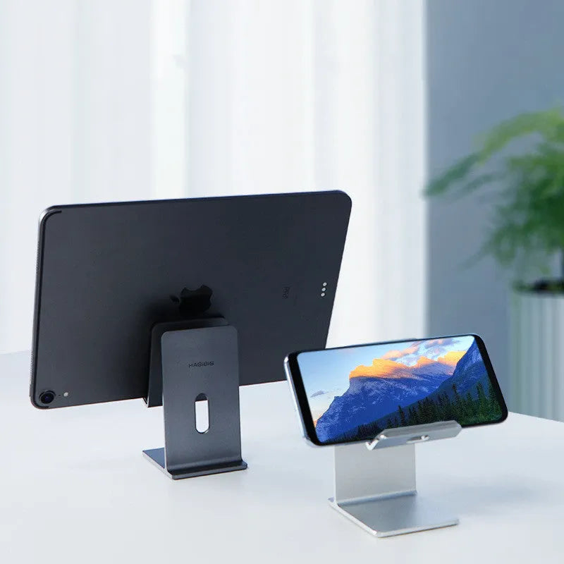 Alloy universal mobile phone and tablet stand in dark space grey colour on a wooden desk.