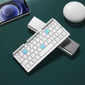 Folded aluminium Bluetooth keyboard showing compact size next to unfolded version with tablet on stand