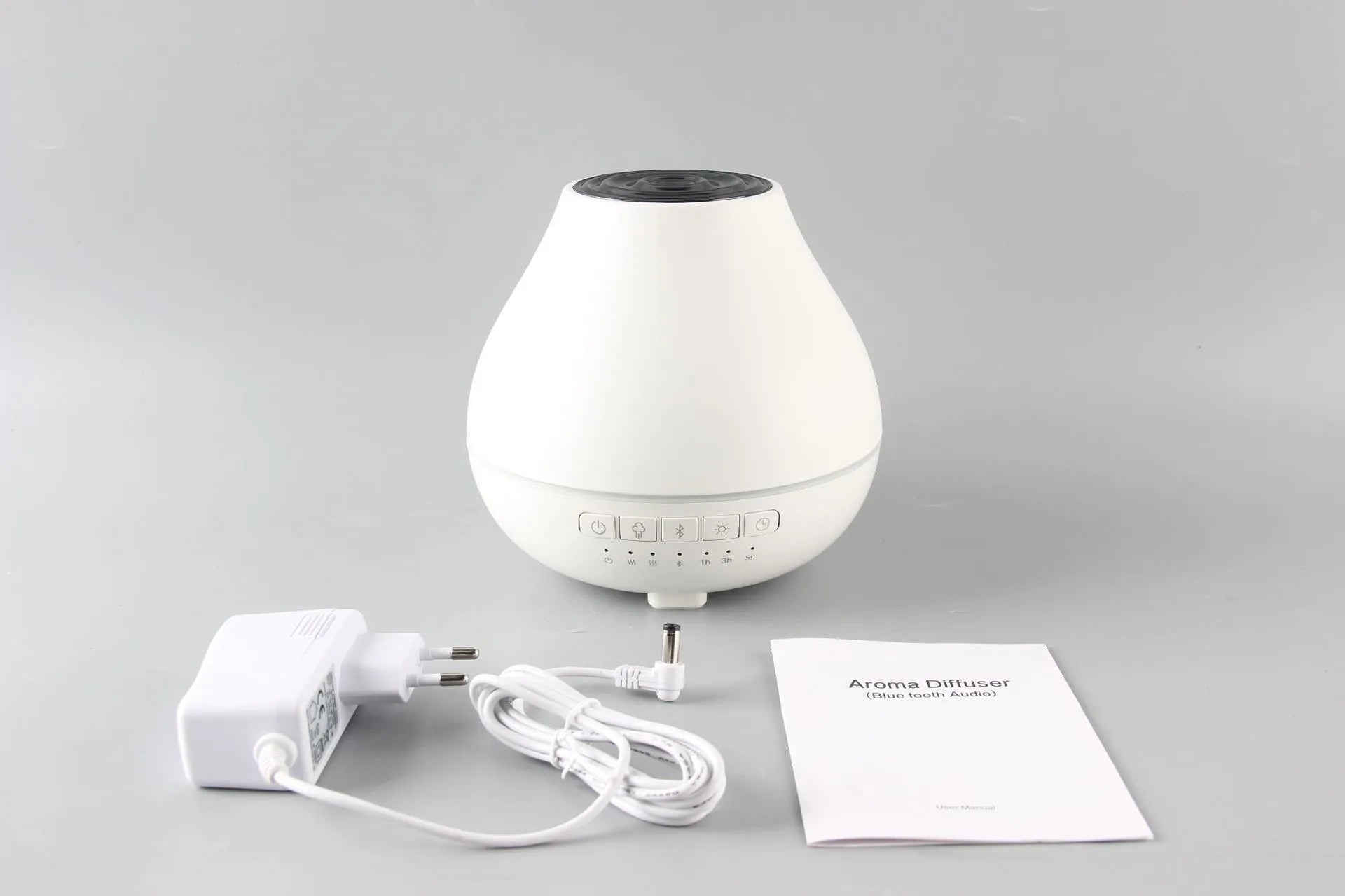 Round white Bluetooth aroma diffuser and humidifier with a colour-changing night light on a table.