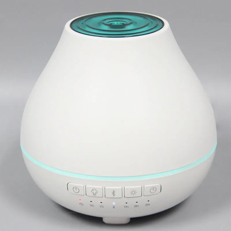 Round white Bluetooth aroma diffuser and humidifier with a colour-changing night light on a table.