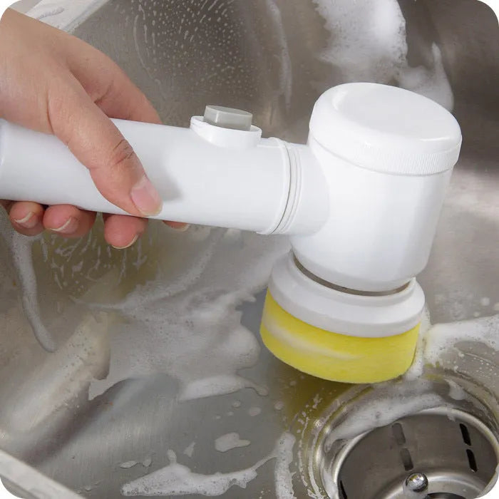 White handheld electric cleaning brush with three interchangeable nylon brush heads on a table.