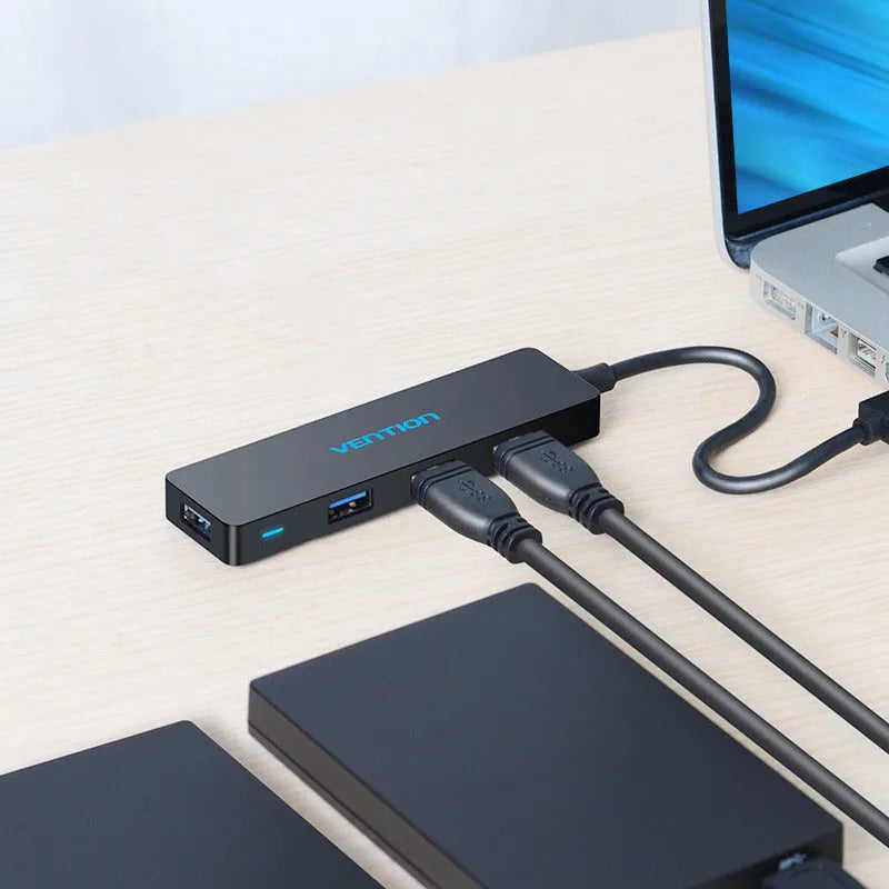 Black 4-port USB 3.0 hub with a short braided cable and nickel-plated connectors on a desk.