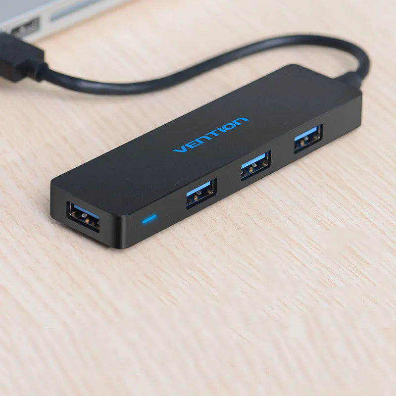 Black 4-port USB 3.0 hub with a short braided cable and nickel-plated connectors on a desk.
