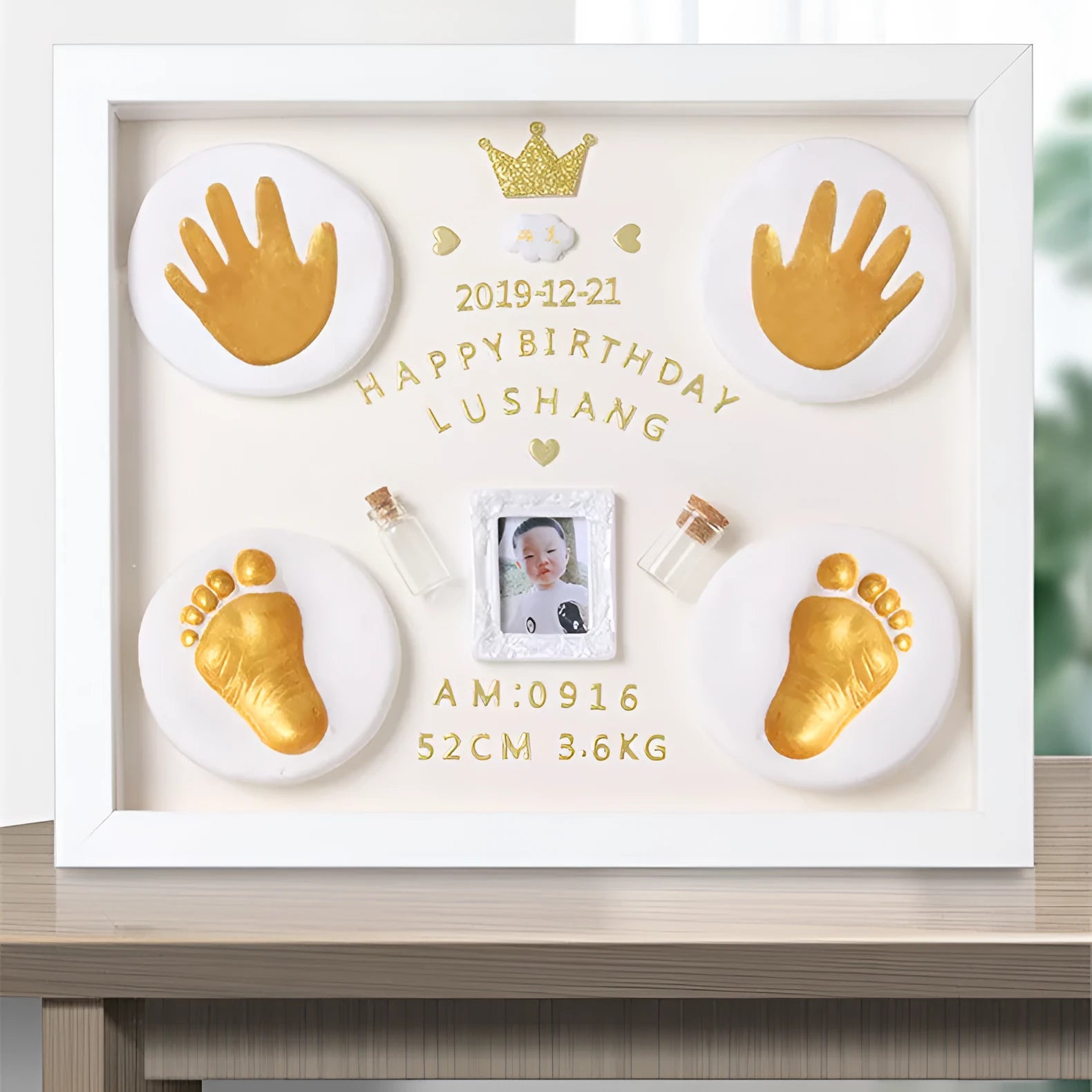 Modern DIY baby hand and foot print anniversary frame in white, shown on a shelf.