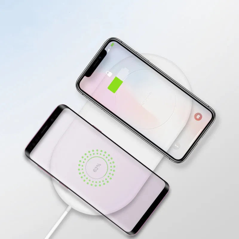 White dual wireless charger charging two mobile phones simultaneously on simple desk