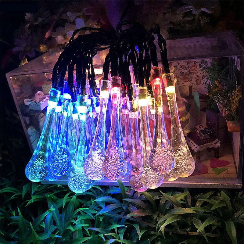 Water drop shaped solar LED fairy lights hanging outdoors with solar panel and ground spike.