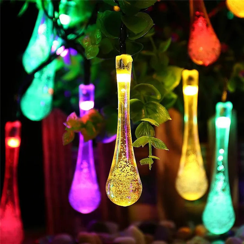 Water drop shaped solar LED fairy lights hanging outdoors with solar panel and ground spike.