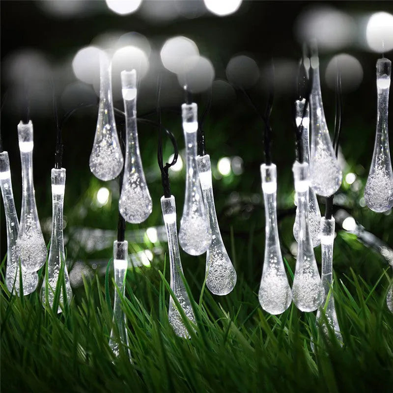 Water drop shaped solar LED fairy lights hanging outdoors with solar panel and ground spike.