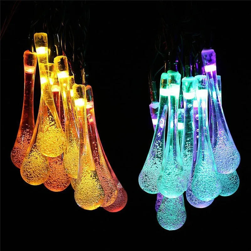 Water drop shaped solar LED fairy lights hanging outdoors with solar panel and ground spike.